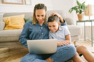A loving mother and her son enjoying a fun time together while using a laptop indoors.
