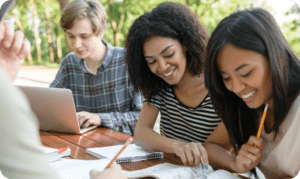 Two students working together on a laptop outdoors, smiling and engaged in learning